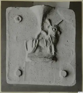 Carved stone relief of a figure on a rectangular stone slab with four small round holes near its corners