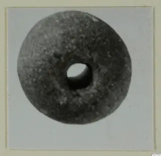 Round disc-shaped object with a large central hole, photographed from above and mounted on a card.