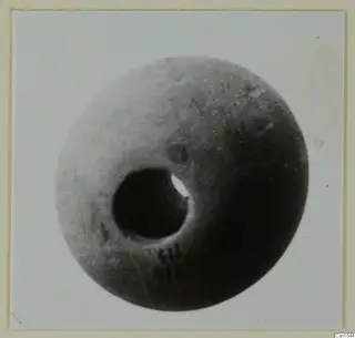 Round object with a large hole through it, a piece of jewellery, shown in a photograph mounted on a card
