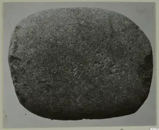 Rounded grey stone object with faint incised marks, photographed flat against a grey backdrop.