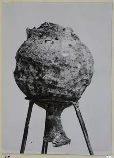 Encrusted rounded vessel with a broken rim and narrow foot, shown on a three-rod stand, from Enkomi
