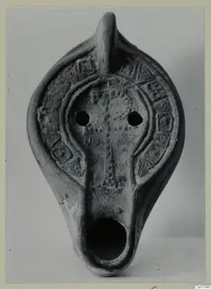 Terracotta oil lamp with a raised cross and rows of dots on the upper surface, seen from the front.