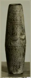 Faience pot with carved bands of pattern, tall tapering form, photographed against a grey backdrop