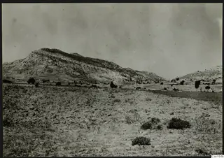 Rocky hill with scattered trees above open scrubby ground at Ayios Iakovos, with small distant figures
