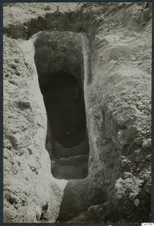Excavated stepped cut at Ayios Iakovos leading down to a dark opening, with stones along the edges