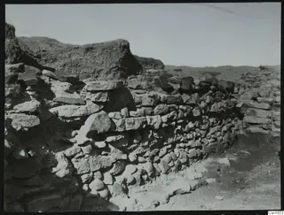 Stone wall foundations at Nitovikla, with rough stones laid in courses against a dry earth bank.