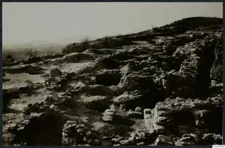 Excavated rock-cut and stone remains on a hillside at Idalion, with low hills in the distance.