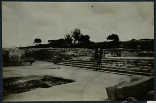 Man in a dark suit holding a cane beside the stone steps at Vouni palace