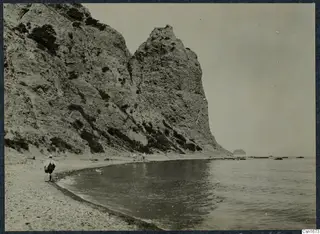Rocky cliff above a pebble beach at Vouni, with a walking figure with a bag and calm sea to the right