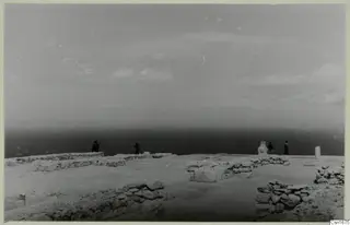 Hilltop view at Vouni Palace with low ruined walls in the foreground and four people standing near the sea edge