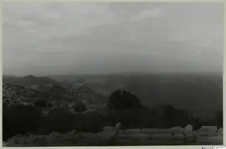 View from Vouni Palace over scrubby hills and trees towards the sea, with stone wall tops in the foreground