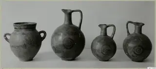 Four painted pots from Marion shown in a row against a grey backdrop, one two-handled jar and three jugs.