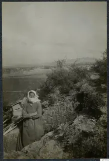 Woman with a white headscarf stands at the edge of a trench at Marion, with a wooden box and poles beside her.