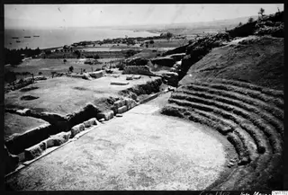 The theatre at Soli, with rows of stone seating curving round a paved floor and the sea beyond.