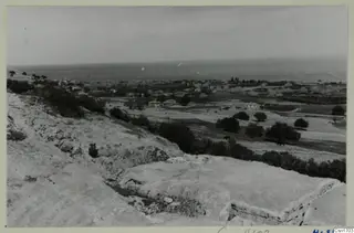 The theatre at Soli: cut stone ledges in the foreground, with a village, fields and the sea beyond
