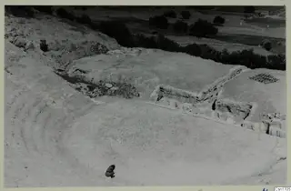 The theatre at Soli, looking down over curved rows of seats, a stone wall and one small figure in the foreground