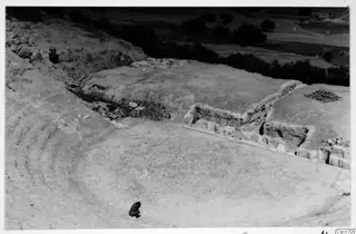 The theatre at Soli, with curved tiered seating, a stone wall with large blocks, and one small crouching figure