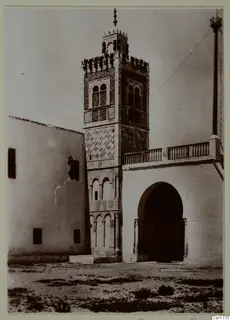 Tall tower with tiled panels beside a whitewashed building with a deep arched doorway