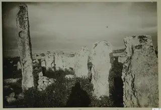 Tall upright stone slabs standing in grass, with scattered rubble and a cloudy sky behind them