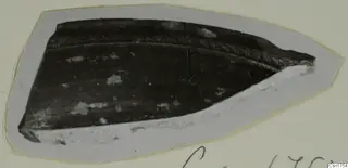 Pottery sherd mounted on grey card, with a dark surface and a raised ridge near one edge.