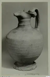 Pottery jug with a pinched spout, single strap handle and ring foot, shown against a grey background