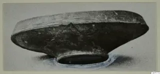 Dark, shallow vessel with a wide body and narrow ring foot, photographed from the side.