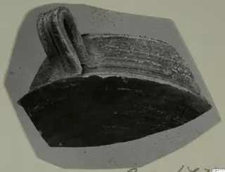 Fragment of a pottery vessel with a ribbed strap handle, shown on a grey card mount.