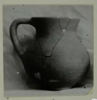Cypro-Hell. II pottery jug with a single handle, cracked and partly broken, against a plain background