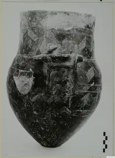 Dark pottery vessel with a rounded body, flaring neck, incised chevron and line patterns, and applied lugs and a bar handle.