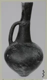 Single-handled polished pottery jug from Vounous, photographed on a grey backdrop beside a scale bar