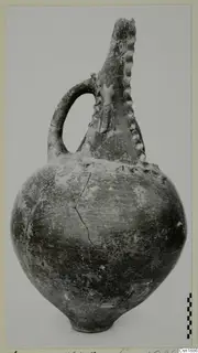 Red Polished I vessel from Vounous with a strap handle and ridged neck, photographed against a plain background.