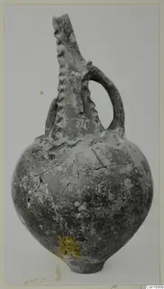 Pottery jug with a tall ridged neck and a single strap handle, photographed against a plain light background.