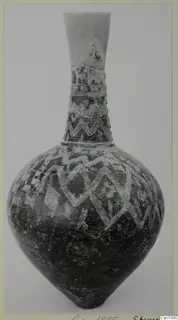 Tall-necked pottery jar with a dark surface and white zigzag and hatched bands, photographed against a plain grey background