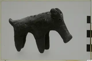 Dark clay animal figure with four tapering legs, a long snout and a short tail, from Vounous.