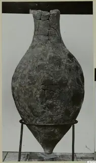 Stone Age pottery vessel with a tall neck and cracked surface, standing on a wire stand