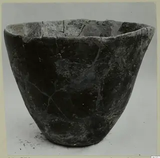 Dark grey bowl with a wide mouth and straight flared sides, its surface cracked and mended, photographed on a plain background.