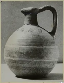 Bichrome-Red pottery jug from Marion with a round body, tall neck and strap handle, against a grey backdrop