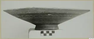 Bichrome-Red pottery bowl with a wavy painted band, photographed on a white plinth beside a checkerboard scale
