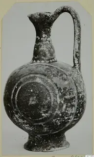 Pottery vessel with a tall neck, strap handle and concentric circles painted on the body