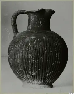 Black-slipped jug with a high loop handle and vertical fluting on the body, photographed against a plain background.