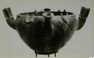 Red Polished III bowl from Vounous, with two large side lugs, a central spout and small knobs on the rim, set on a metal stand.