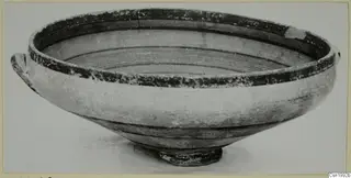 Pottery bowl with two small handles and dark painted bands around the rim and interior, shown on a plain background