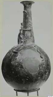 Red Polished II jug from Vounous, with a globular body, tall neck and raised relief decoration, standing on a wire stand.