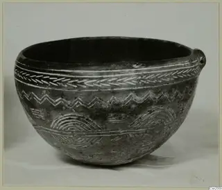 Dark rounded bowl with a small lug on one side and white-filled incised bands of chevron and zigzag decoration, from Lapithos