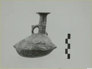 Pottery vessel with a flaring neck and loop handle, painted with lattice and hatched bands, beside a scale bar