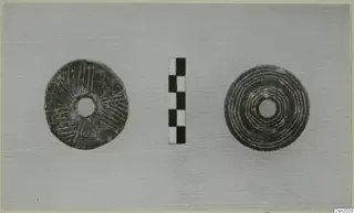 Two flat discs with central holes, one with radiating incised lines and one with concentric rings, beside a checkered scale bar