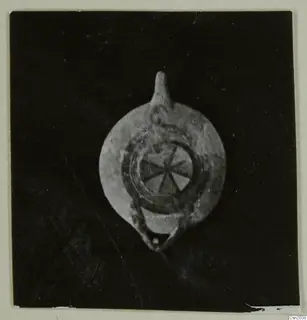 Pottery oil lamp with a nozzle at the top and a radial pattern on its disc, shown against a dark background