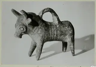 Clay bull-shaped vessel with a loop handle over its back, photographed against a pale grey background.
