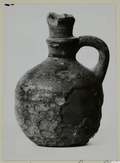 Small jug with a single loop handle and a broken rim, photographed against a plain background.