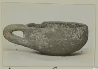 Small pottery bowl with a single loop handle, seen from the side.